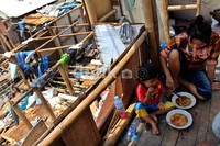 Seorang ibu beserta anaknya makan di antara rumahnya yang tergusur.