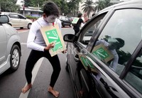 Seniman pantomim menunjukan poster sopan-santun merokok di tempat umum kepada pengendara yang melintas.