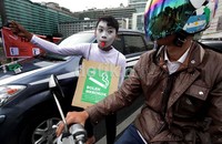 Seniman pantomim menunjukan poster sopan-santun merokok di tempat umum kepada pengendara yang melintas.