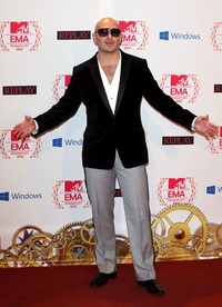 Pitbull berpose dengan kemeja putih, jas hitam, dan celana abu-abu saat di red carpet. Tim Whitby/Getty Images for MTV.