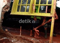 Seorang warga membersihkan lumpur dan juga puing di depan rumahnya.