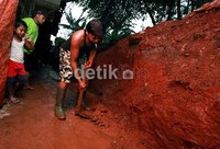 Seorang warga membersihkan lumpur di depan rumahnya.