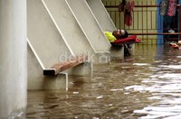 Seorang warga menunggu banjir surut sambil tuduran di depan rumahnya yang tergenang. Ramses/detikcom.