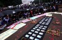 Para pendemo yang membawa payung berwarna hitam duduk-duduk di sekitar topeng dan poster tuntutan.