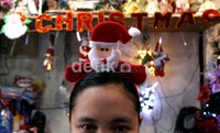 Penjaga toko yang memakai ikat kepala santa klaus menyambut pembeli yang akan berbelanja pernak-pernik Natal.