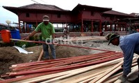 Dua orang pekerja menyiapkan kayu-kayu yang akan digunakan untuk merenovasi rumah Si Pitung.