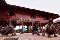 Tiga orang pekerja memasang keramik di lantai rumah Si Pitung.