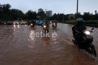 Beberapa kendaraan roda dua berusaha melintasi genangan air yang tinggi.