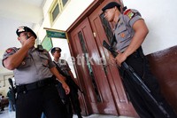 Polisi bersenjata berjaga di depan pintu masuk ruang sidang.