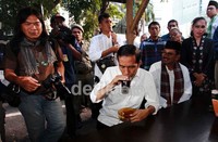 Jokowi berdiskusi dengan pewarta foto sambil menyeruput kopi.