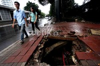 Dua pejalan kaki menghindari lubang besar yang menganga saat berjalan di pendestrian Jalan Gatot Subroto, Jakarta.