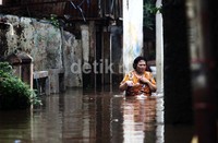 Seorang ibu benrjalan di genagan banjir sepinggang.     