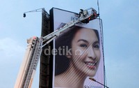 Petugas yang berdiri di atas crane mengendorkan baut-baut yang ada di reklame itu.