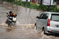 Seorang pengendara, tetap berkomunikasi dengan ponselnya, saat mendorong kendaraan motornya melintasi genangan banjir.