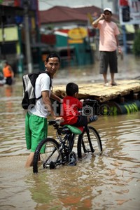 Seorang ayah membawa anaknya melintasi banjir dengan sepeda.