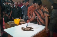 Seorang pelukis tengah menunjukan cara membuat lukisan dengan bubuk teh.