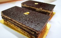 Opera cake di Bakerzin terdiri dari 3 lapis sponge cake yang lebih kasar dan berongga, namun siraman coffee syrup membuatnya jadi lebih lembut. Di atasnya diberikan sedikit gold leaf yang membuatnya tampak mewah.