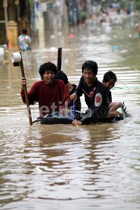 Beberapa warga menyeberangi jalanan yang terendam menggunakan ban.