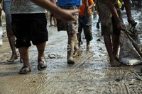 Warga bergotong royong membersihkan lumpur yang menumpuk di jalan.