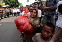 Seorang ibu membawa makanan yang dibungkus dalam kantong plastik.