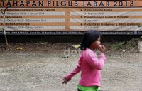 Seorang anak melintas di depan spanduk Tahapan Pilgub Jabar 2013, yang dipasang di halaman Kelurahan Kayuringin Jaya.