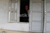 Seorang bapak melihat genangan dari balik jendela.