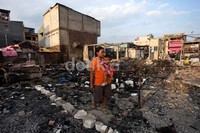 Seorang warga berdiri di depan rumahnya yang hangus terbakar.