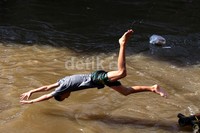 Seorang anak melakukan atraksi salto. Dia tidak mempedulikan derasnya arus yang mengancam keselamatan.