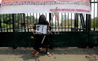Salah satu pendemo yang memakai kostum serba hitam membentangkan poster di depan gerbang gedung DPR.