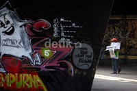 Seorang pedagang koran melintas di depan mural.