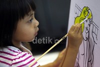 Seorang anak menunjukkan tingkat kreativitasnya, dengan fokus mewarnai gambar di atas kanvas.