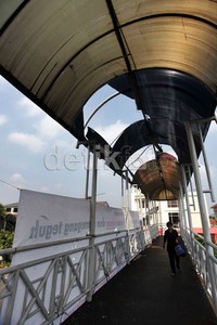 Seorang pejalan kaki melintas di JPO yang kondisi atapnya bolong.