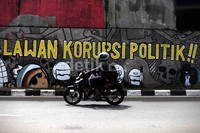 Pengendara melintas di mural bertema korupsi.
