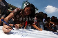 Para siswa membubuhkan tanda tangan di sebuah kain putih yang dibentangkan di halaman sekolah.