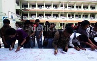 Para siswa meluapkan kegembiraan dengan membubuhkan tanda tangan di kain raksasa di halaman sekolah.