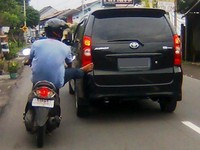 Pengendara motor meletakkan kaki kanannya di bodi mobil, terlihat seperti sedang berusaha mendorong mobil. (Foto Amanuharis)