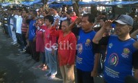 Puluhan pedagang yang sedang menjaga kios terlihat membentuk barisan di depan tiang bendera. Busana mereka seadanya, berkaos bahkan beralas kaki sandal.