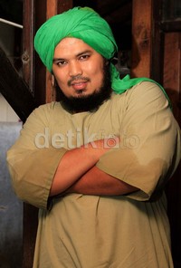 Ia terlihat mengenakan gamis berwarna cokelat, dan di kepalanya terpasang sorban hijau muda.