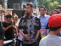 Ia terlihat mengenakan kemeja hitam bermotif bunga.