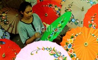 Seorang perajin payung ritual sedang melukis ornamen hias pada bidang payung yang terbuat dari kertas semen.