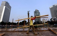 Seorang pekerja menyiapkan kayu-kayu yang akan digunakan untuk membuat pembatas di sekeliling kolam.