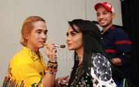 Bibirnya dipoles lipstik merah, kontras dengan rambut hitam panjangnya yang tertata rapi.