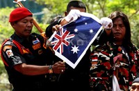Pendemo membakar kertas bergambar bendera Australia.