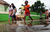 Tiga orang warga melintas di jalanan yang terendam banjir.