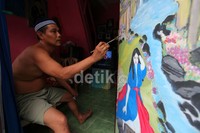 Seorang warga melukis tembok rumahnya.