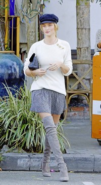 Rosie Huntington-Whiteley menghadirkan nuansa 90-an lewat sweater putih, rok mini bermotif, knee-high boot dan topi cap.