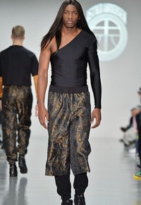 Masih di koleksi Astrid Andersen, kini atasan pas badan dengan lengan one shoulder yang ditampilkan. Atasan ketat itu dipadukan bersama celana bermotif keemasan.