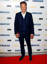 Aktor Richard E Grant yang tampil mengenakan setelan jas bermotif kotak-kotak ini nampak necis di atas red carpet. Anthony Harvey/Getty Images.