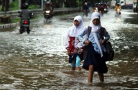 Dua orang pelajar melintas di jalanan yang terendam banjir.