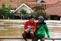 Dua orang warga asyik berbincang sambil menunggu banjir surut.